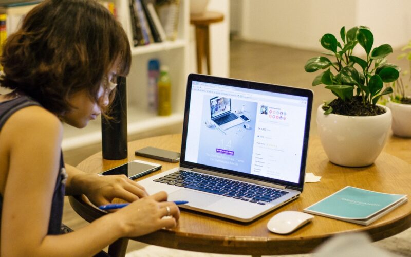 Young woman is working at the table with pen near an open MacBook and a mouse.